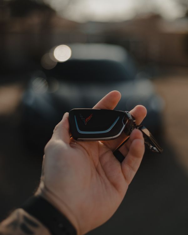 A hand holding an original Chevrolet Corvette key fob outdoors.