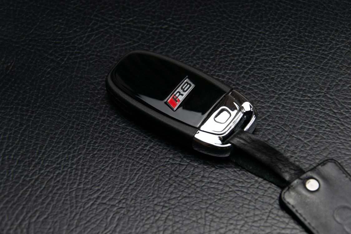 An original Audi R8 key fob resting on a leather surface.