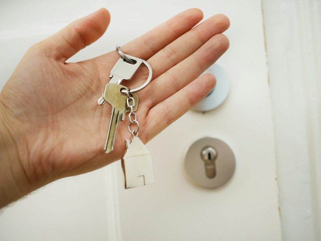 A hand holding real house keys beside a front door lock.