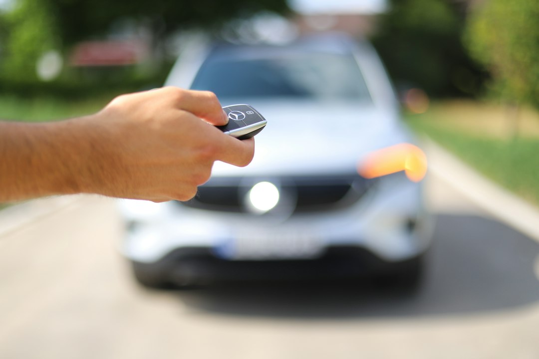 A hand holding an original Mercedes-Benz key fob beside a vehicle.